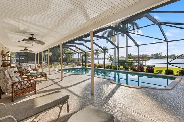 view of swimming pool with a patio area, a water view, glass enclosure, ceiling fan, and an outdoor living space