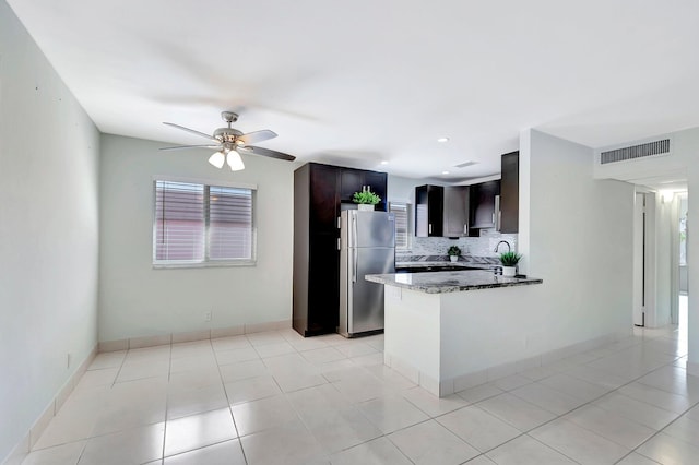 kitchen with stainless steel fridge, tasteful backsplash, dark brown cabinetry, kitchen peninsula, and dark stone counters