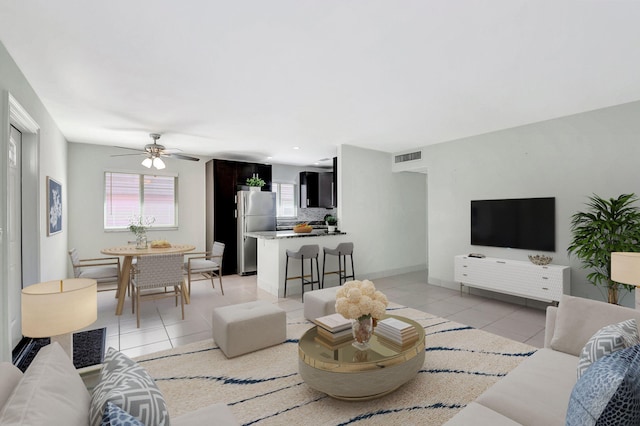 living room with light tile patterned floors, a ceiling fan, visible vents, and baseboards