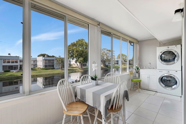 sunroom featuring tile patterned flooring, stacked washer / drying machine, a water view, and a sink