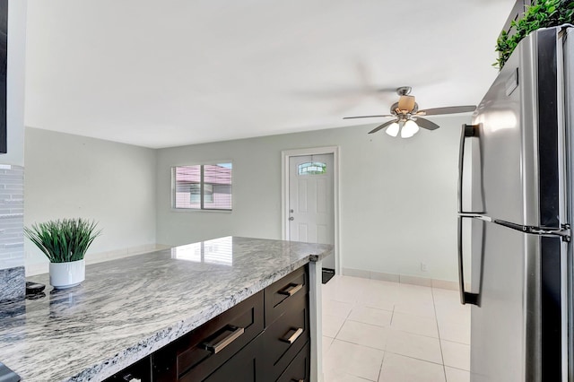 kitchen with baseboards, ceiling fan, light tile patterned floors, light stone counters, and freestanding refrigerator