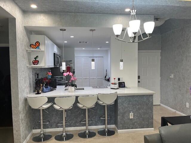 kitchen featuring pendant lighting, white cabinetry, stove, an inviting chandelier, and kitchen peninsula