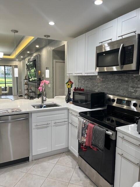 kitchen featuring sink, light tile patterned floors, appliances with stainless steel finishes, white cabinetry, and hanging light fixtures