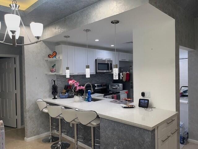 kitchen with appliances with stainless steel finishes, decorative light fixtures, kitchen peninsula, and white cabinets