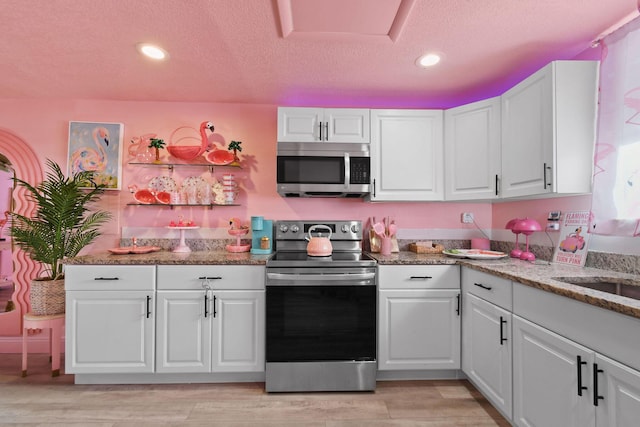 kitchen featuring stone counters, appliances with stainless steel finishes, light wood-type flooring, and white cabinets