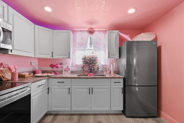 kitchen with stainless steel appliances, white cabinetry, sink, and light wood-type flooring