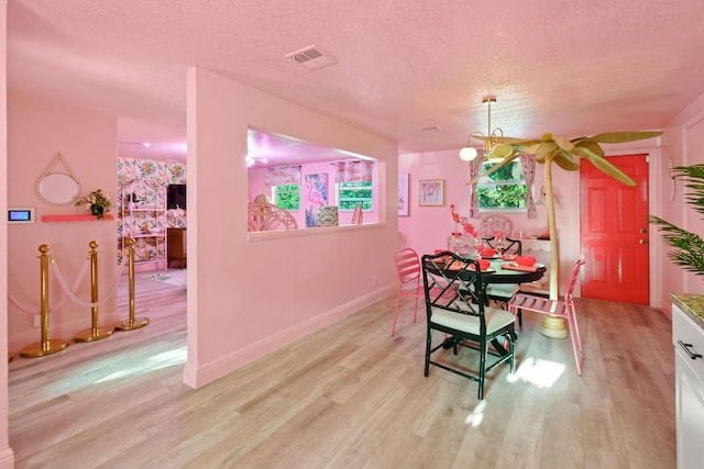 dining area featuring an inviting chandelier, light hardwood / wood-style flooring, and a textured ceiling