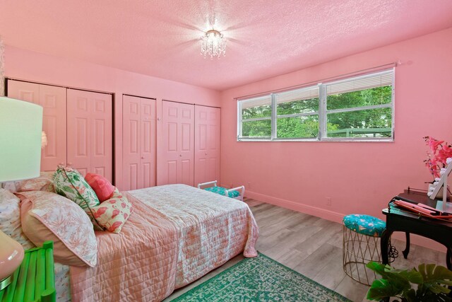 bedroom featuring two closets, a textured ceiling, and light wood-type flooring