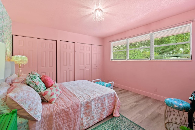 bedroom featuring two closets, a textured ceiling, and light wood-type flooring