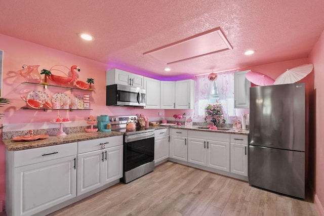 kitchen with white cabinetry, sink, dark stone counters, stainless steel appliances, and light wood-type flooring