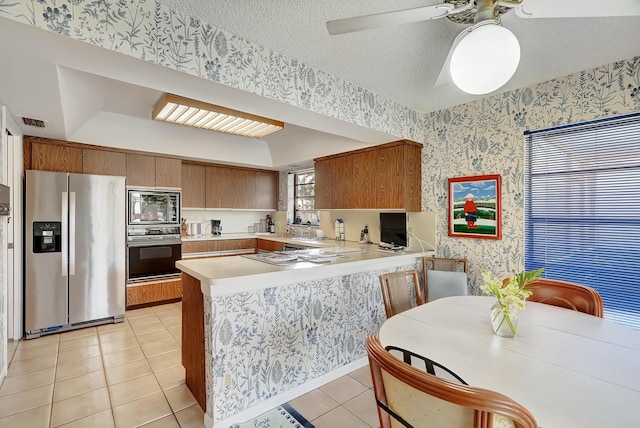 kitchen featuring light tile patterned flooring, kitchen peninsula, a textured ceiling, and appliances with stainless steel finishes