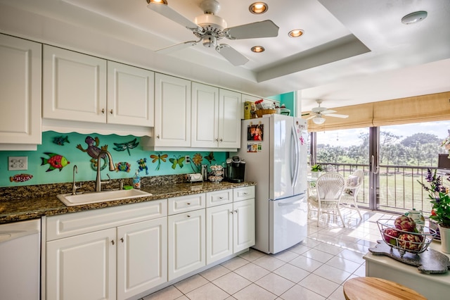 kitchen with sink, dark stone countertops, white cabinets, a raised ceiling, and white appliances