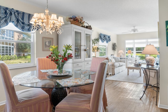 dining space with ceiling fan with notable chandelier, light hardwood / wood-style flooring, and a textured ceiling