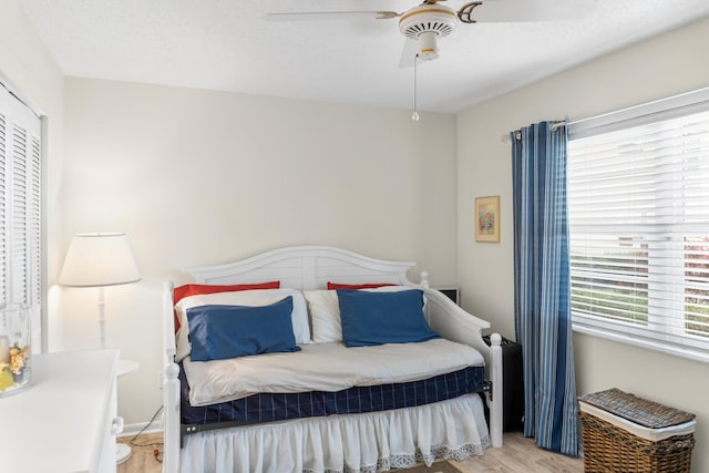 bedroom with ceiling fan, light hardwood / wood-style floors, multiple windows, and a textured ceiling