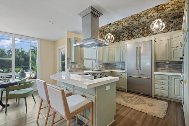 kitchen featuring sink, dark wood-type flooring, built in refrigerator, hanging light fixtures, and island exhaust hood