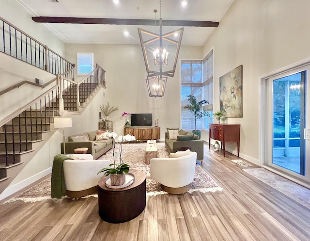 living room featuring beamed ceiling, a towering ceiling, a chandelier, and light hardwood / wood-style floors