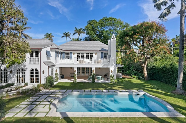 rear view of property with french doors, a patio, a balcony, and a lawn