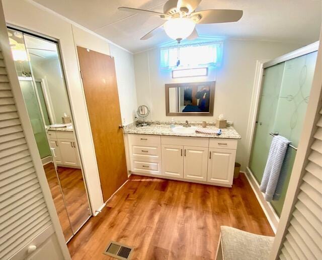 bathroom featuring wood-type flooring, ornamental molding, vanity, a shower with door, and ceiling fan