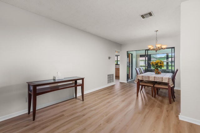 dining space with a textured ceiling, a notable chandelier, and light wood-type flooring