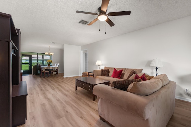 living room with ceiling fan with notable chandelier, light hardwood / wood-style floors, and a textured ceiling