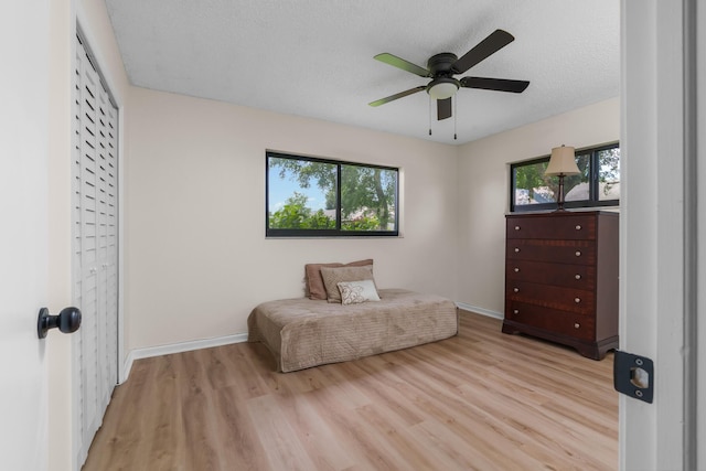 living area with ceiling fan, a textured ceiling, and light hardwood / wood-style flooring