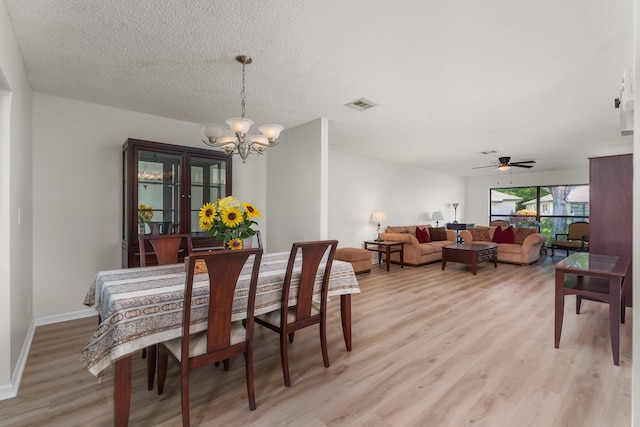 dining area with light wood-type flooring, a textured ceiling, and a notable chandelier