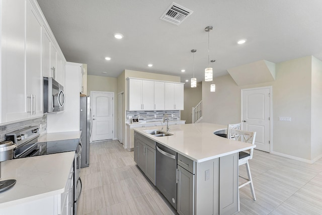 kitchen with sink, decorative light fixtures, a center island with sink, stainless steel appliances, and white cabinets