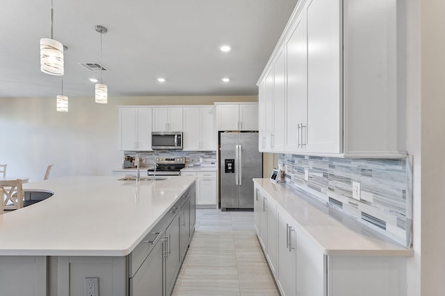 kitchen featuring pendant lighting, stainless steel appliances, an island with sink, and white cabinets