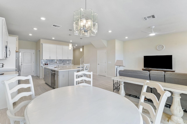 dining room with sink, ceiling fan with notable chandelier, and light wood-type flooring