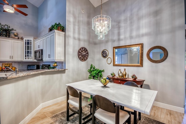 dining area featuring sink, a towering ceiling, ceiling fan with notable chandelier, and light wood-type flooring