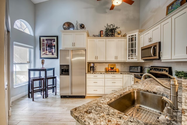 kitchen with sink, backsplash, a high ceiling, stainless steel appliances, and light stone countertops