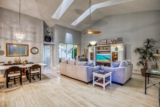 living room with ceiling fan with notable chandelier, high vaulted ceiling, a skylight, and light hardwood / wood-style floors