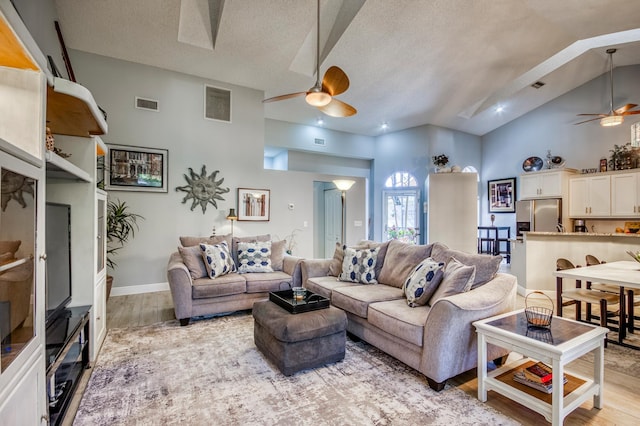 living room featuring high vaulted ceiling, a textured ceiling, ceiling fan, and light hardwood / wood-style flooring