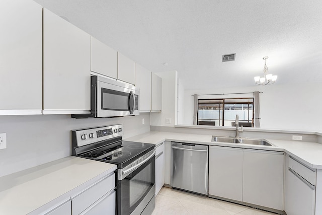 kitchen with appliances with stainless steel finishes, white cabinetry, sink, light tile patterned floors, and a textured ceiling