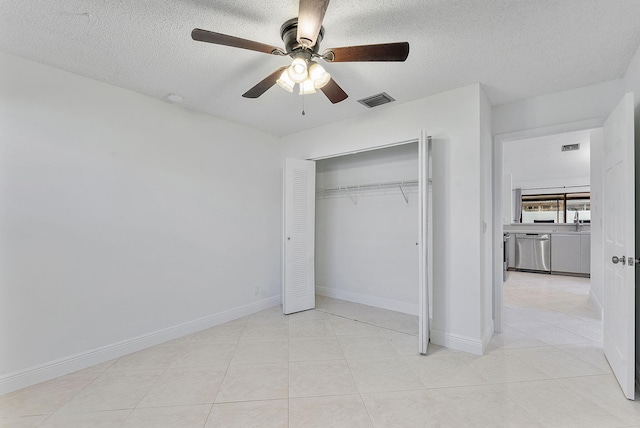 unfurnished bedroom featuring ceiling fan, a closet, a textured ceiling, and light tile patterned floors