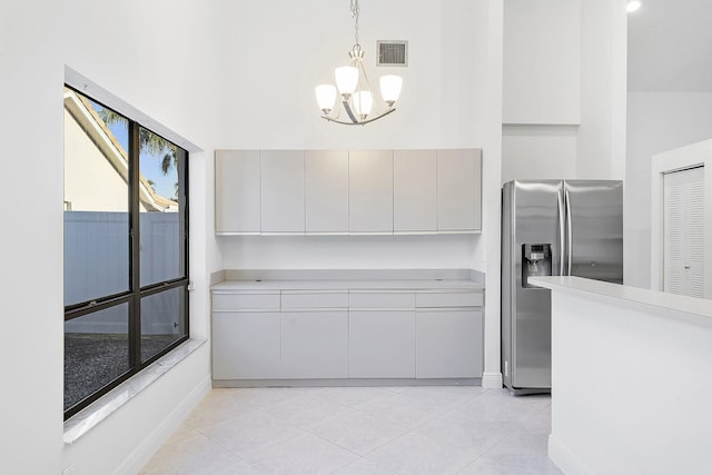 kitchen with a towering ceiling, pendant lighting, light tile patterned floors, and stainless steel fridge with ice dispenser