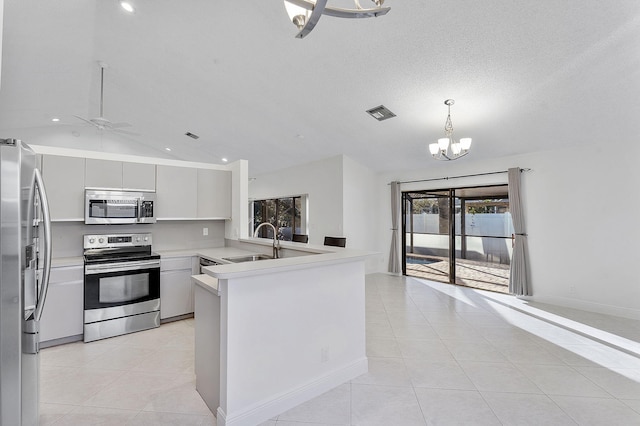 kitchen with light tile patterned flooring, vaulted ceiling, sink, kitchen peninsula, and stainless steel appliances