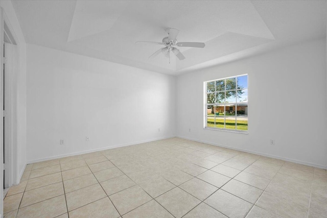 tiled empty room with a raised ceiling and ceiling fan