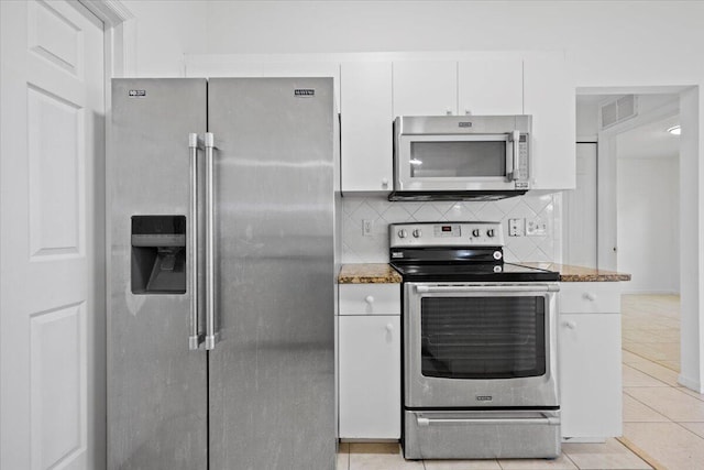 kitchen featuring light tile patterned flooring, dark stone countertops, appliances with stainless steel finishes, white cabinets, and backsplash