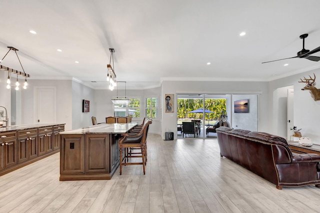 kitchen with a kitchen island, a breakfast bar, hanging light fixtures, light stone countertops, and light hardwood / wood-style flooring