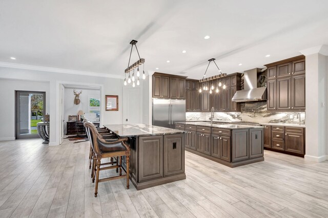 kitchen with wall chimney range hood, a center island, dark brown cabinetry, decorative light fixtures, and stainless steel built in fridge