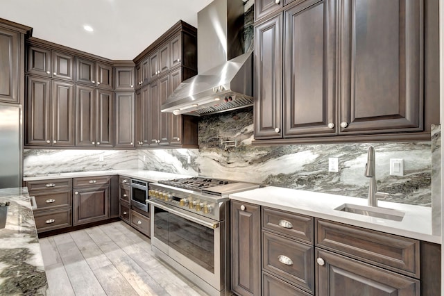 kitchen featuring appliances with stainless steel finishes, sink, dark brown cabinets, and wall chimney range hood