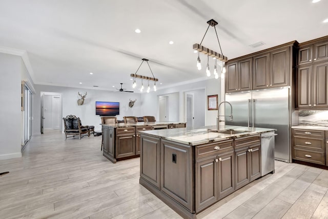 kitchen featuring a kitchen island with sink, sink, decorative light fixtures, and dark brown cabinets