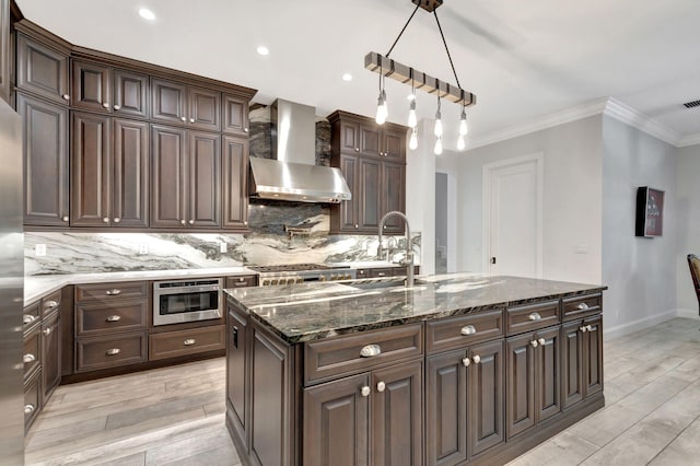 kitchen featuring sink, dark brown cabinets, decorative backsplash, decorative light fixtures, and wall chimney exhaust hood