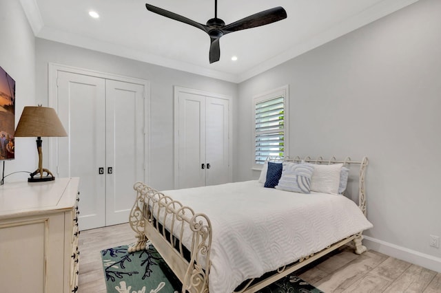 bedroom with two closets, ornamental molding, light hardwood / wood-style floors, and ceiling fan