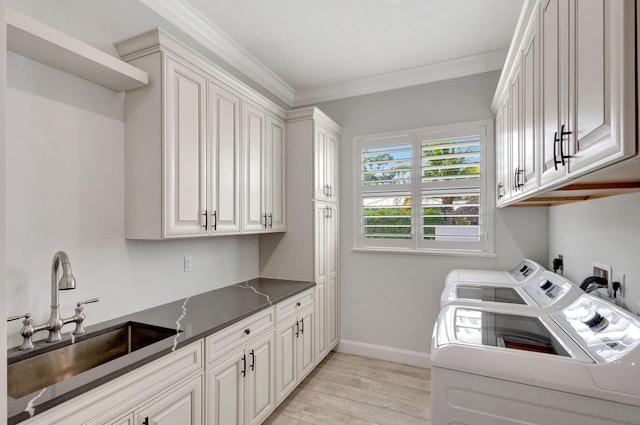 clothes washing area with sink, washing machine and dryer, cabinets, ornamental molding, and light hardwood / wood-style floors