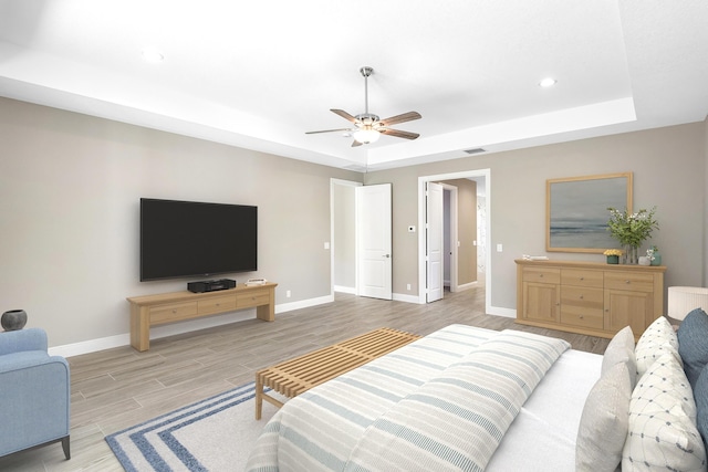 bedroom with a raised ceiling, ceiling fan, and light wood-type flooring