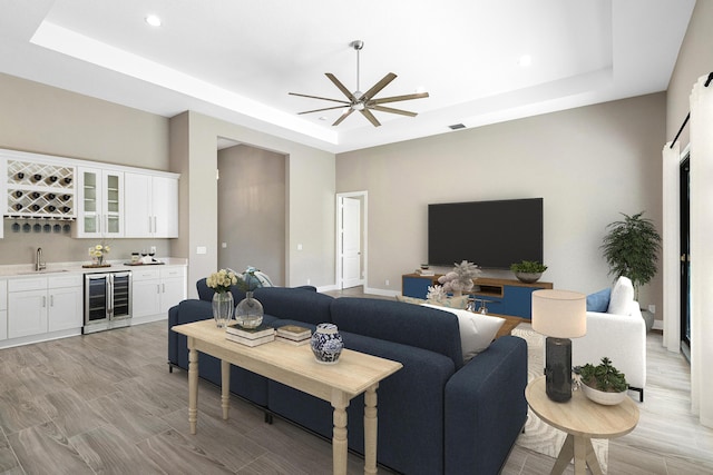 living room with ceiling fan, wine cooler, a tray ceiling, indoor wet bar, and light wood-style floors