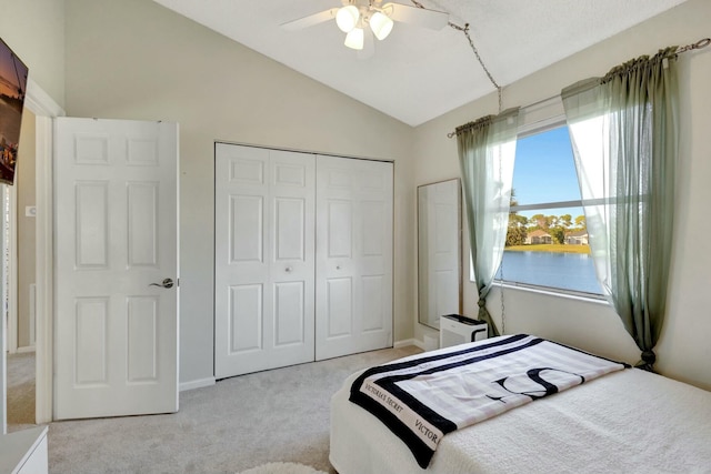 bedroom with a water view, a closet, vaulted ceiling, ceiling fan, and light carpet