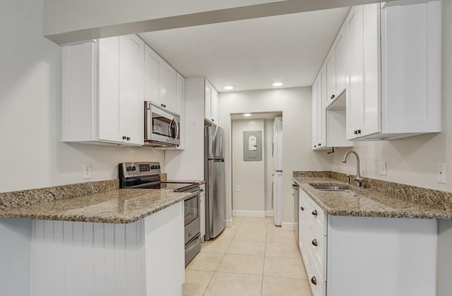 kitchen with light stone countertops, appliances with stainless steel finishes, light tile patterned flooring, white cabinetry, and a sink